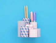 A completed DIY pencil holder laid on a blue background, with three coloured markers inside.